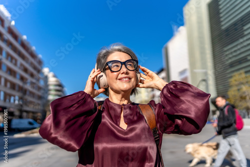 Foto Mature woman enjoying music listening headphones city street