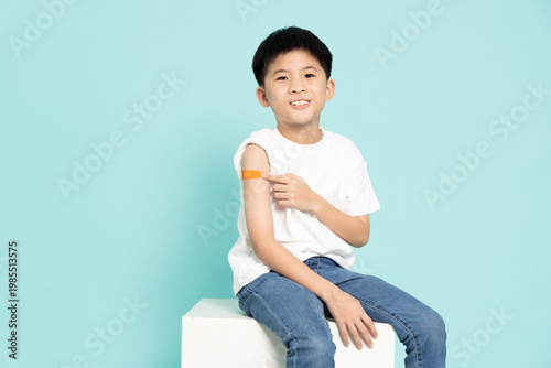 Obraz na plátně A smiling young Asian boy confidently sitting and shows off a bandage on his upper arm after receiving a vaccination isolated on green background