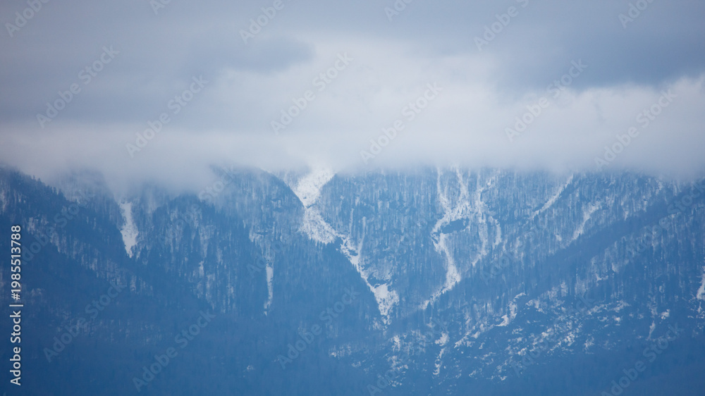 Fototapeta premium Snow-capped mountains partially hidden by clouds