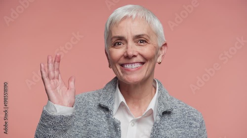 Senior woman waving hello with smile on pink background