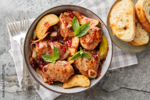 Close-up of seared and then braised pork tenderloin with caramelized onions, cranberry sauce and green apples in a bowl on the table. Horizontal top view from above