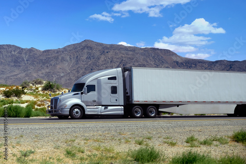 semi truck driving on highway through green nature and mountains. Commercial vehicle transport for logistics and freight shipping.