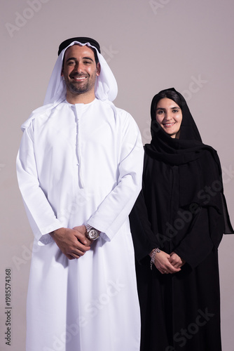 Emirati couple in traditional clothing smiling for a studio portrait on a neutral background