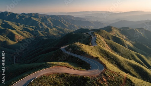 Winding road snakes through rolling green hills under soft sunrise light