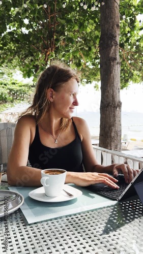 Woman working on tablet with keyboard while sitting outdoor cafe. Enjoying coffee and peaceful atmosphere under green trees, combining remote work, travel lifestyle and relaxation in sunny environment