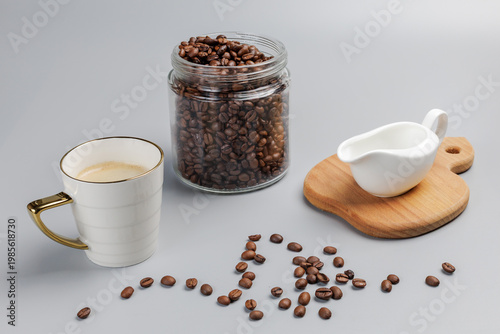 Cup of coffee, a glass can with roasted coffee beans and a cream sauceboat.