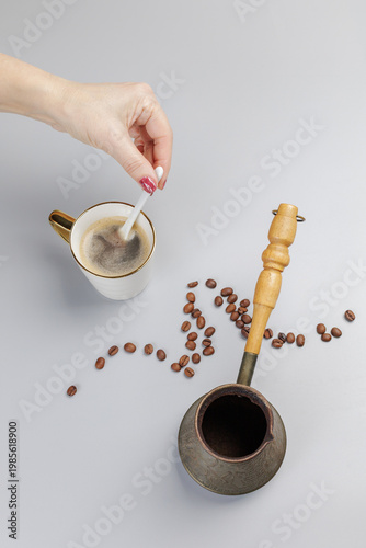 Cezve with roasted coffee beans and a woman's hand with a spoon and a cup of coffee.