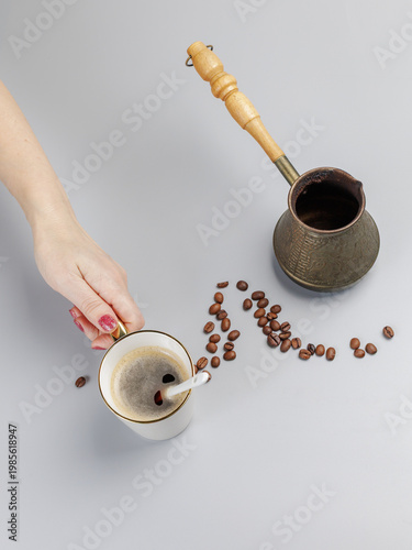 Cezve with roasted coffee beans and a woman's hand with a cup of coffee.