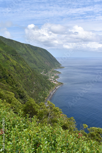 View of forested steep slopes with a small village on the coast, ocean waves, Sao Jorge Island, Azores