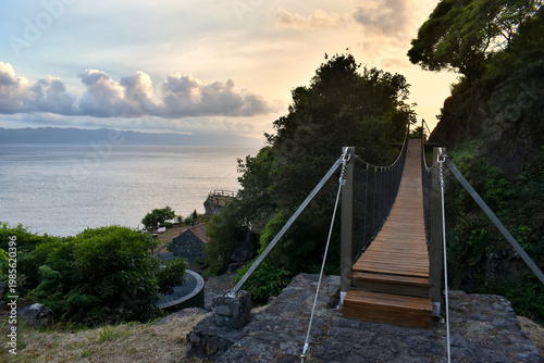 Suspension rope bridge over a small gorge, sunset in the background, Azores