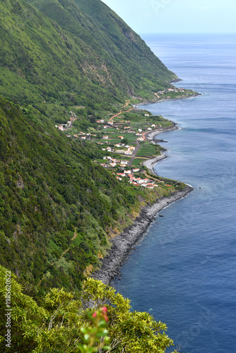 View of forested steep slopes with a small village on the coast, ocean waves, Sao Jorge Island, Azores