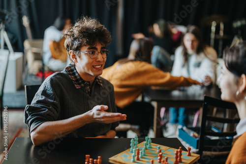 Cuadro en lienzo A young male student gestures while talking to a fellow student over a chessboard