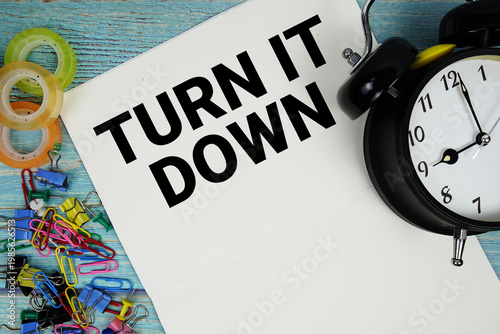 Turn It Down text with alarm clock and colorful office supplies on a blue wooden surface
