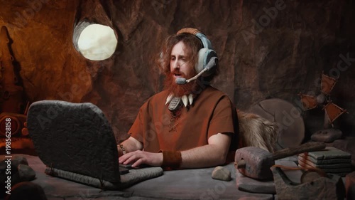 Caveman customer service agent with headset working on a stone laptop in his cave office.