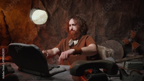 Enthusiastic caveman businessman making a phone call on a stone handset while working on his laptop