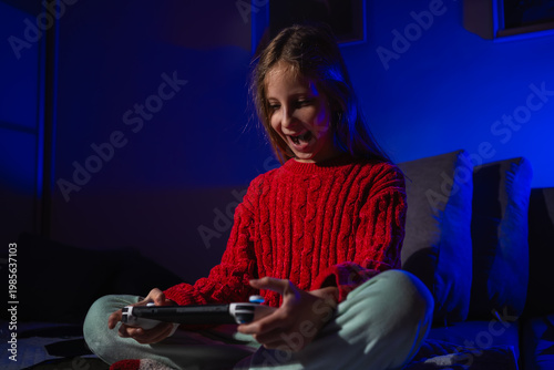 Excited laughing girl reacting to a game on her portable console in a dark bedroom with blue light