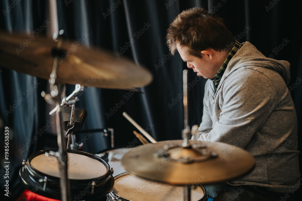 Obraz premium A male drummer practices on a drum kit, concentrating on his playing. The focused student musician rehearses in a dim studio setting.