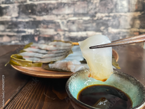 Foto サワラとアオリイカの昆布締め。新鮮な刺身を昆布で包んで熟成させた料理。アオリイカに醤油をつけて食べるところ。