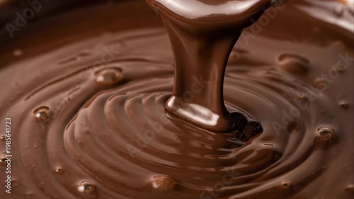 Melted dark chocolate pouring from a spoon into a bowl. Smooth liquid cocoa texture and ripple surface details. Culinary ingredient for dessert preparation and sweet confectionary food.