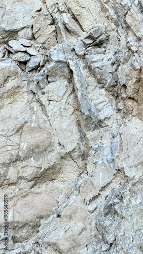 Vertical close-up shot of a heavily fractured limestone rock surface with angular chunks, veins, and layered breaks in shades of beige, cream, and light gray. 