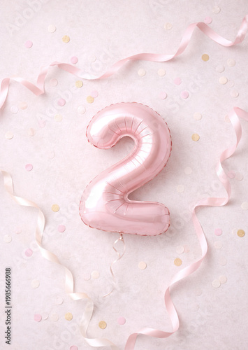 Pink number two balloon with confetti and ribbons on pastel background