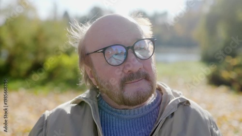 Elderly man relaxes in nature, seated on a bench in an autumn park