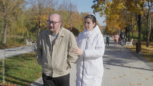 Senior man on autumn walk with supportive caregiver, elder care