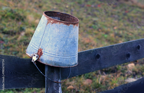 Old rusty metal bucket resting on a weathered wooden fence post in the countryside