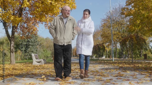 Elderly man with glasses takes a walk with his caregiver in park