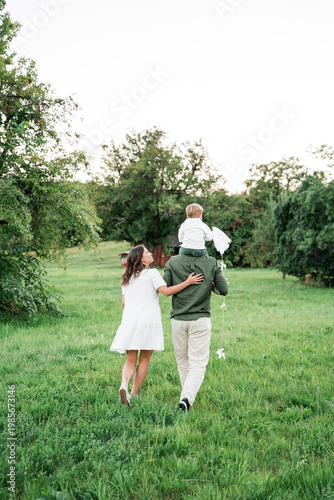 Happy young family with little son playing with kite in field. Healthy childhood.