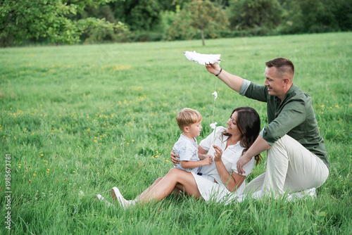 Happy young family with little son playing with kite in field. Healthy childhood.