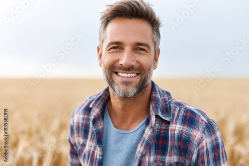 Smiling middle aged man in plaid shirt standing in golden wheat field on a bright day