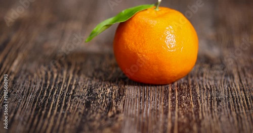 ripe orange tangerine with one green leaf, fruit on a wooden table, unpeeled ripe orange-skinned small tangerine with a long green leaf