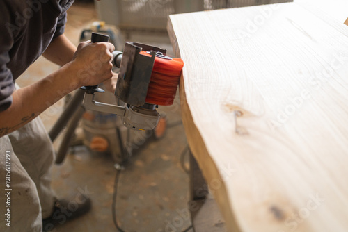 Woodworker sanding natural live edge wood slab in workshop
