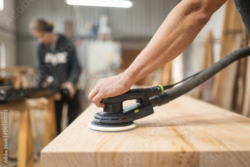 Carpenter sanding wood surface using power tool in workshop