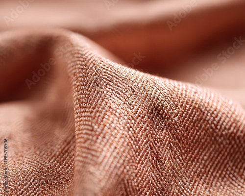 Close up of textured peach colored woven fabric with a herringbone pattern and subtle shimmering threads showing fine detail and soft folds under natural light perfect for textile design and fashion