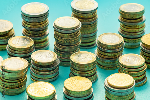 Stacks of coins next to each other, on light blue surface. Amount of money and wealth.