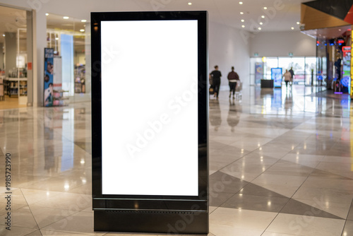 Obraz na płótnie A blank white vertical digital billboard lightbox display stand mockup in a modern Australian shopping centre mall corridor, with blurred shoppers and retail stores in the background