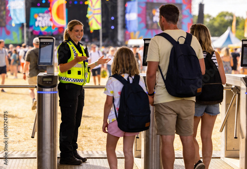 Smiling female security officer greeting a family at music festival entrance gates, event safety and crowd management for outdoor summer concert