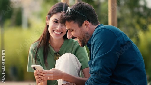 Video of lovely couple talking and laughing while looking together at smartphone in a park