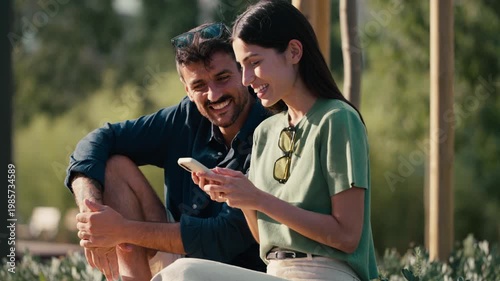 Video of lovely couple talking and laughing while looking together at smartphone in a park