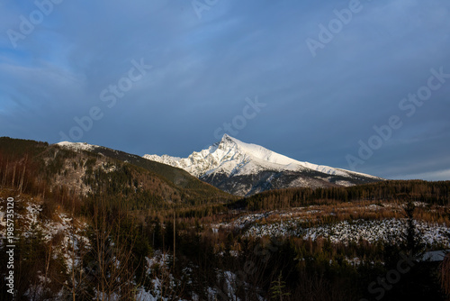 Sunlit snowy mountain peak with dramatic sky over winter landscape