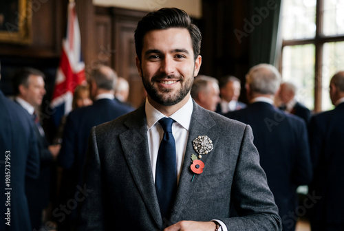 Smiling man in a grey wool suit wearing a red remembrance poppy and an ornate vintage brooch during a formal Memorial Day event.