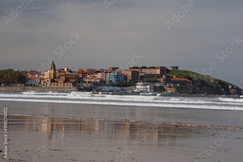 San Pedro Church and San Lorenzo beach with surfers at sunset in Gijon, Asturias, Spain.