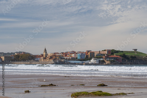 San Pedro Church and San Lorenzo beach with surfers at sunset in Gijon, Asturias, Spain.