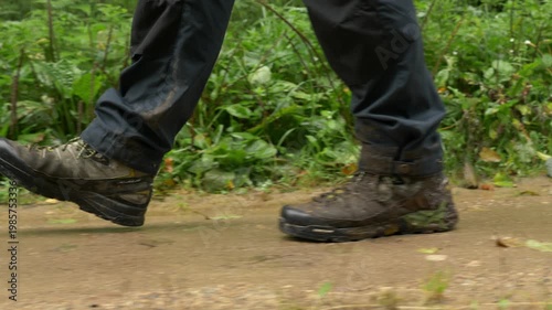 Close‑up of hiker’s boots walking on muddy forest trail after rainfall