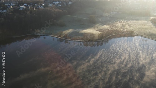 Aerial drone footage capturing early morning fog drifting over a lake in Stavanger, Norway during springtime. The scene features soft mist, calm water, and gentle morning light, creating a quiet and a