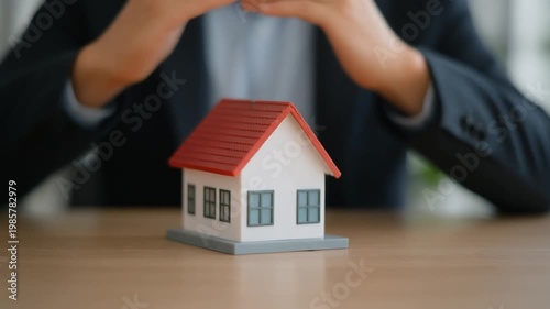 Man's Hands Protecting Miniature House Model on Wooden Table Illustrating Home Insurance and Property Security
