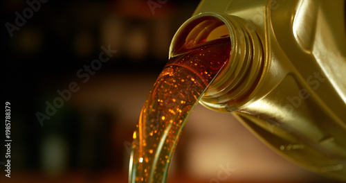 Close-up of motor oil pouring from a plastic container. Golden viscous liquid with bubbles flowing smoothly, automotive maintenance concept with shallow depth of field.