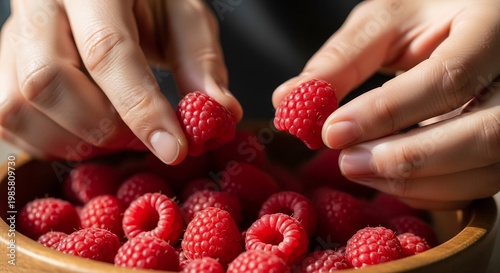 Close-up of hands picking fresh ripe raspberries from a wooden bowl.